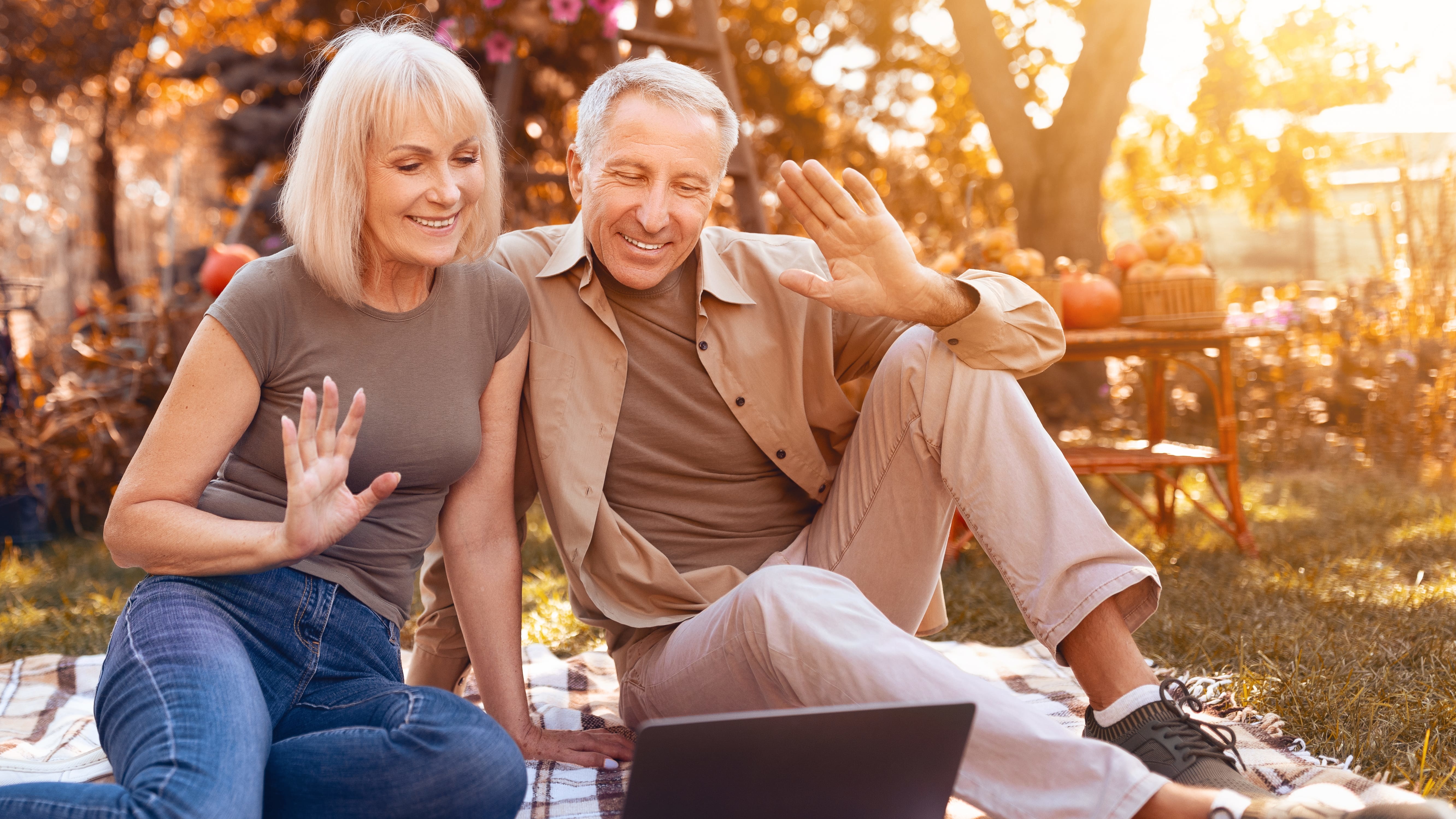 Older couple outside and waving at a computer screen.